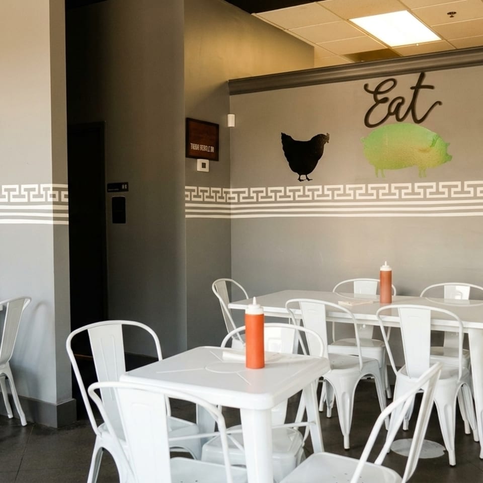 Restaurant interior with white tables and chairs, gray walls with animal silhouettes, and hot sauce bottles.