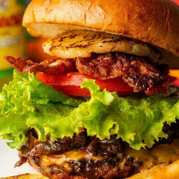 Close-up of a burger with pineapple, bacon, tomato, lettuce, and cheese, served with fries.